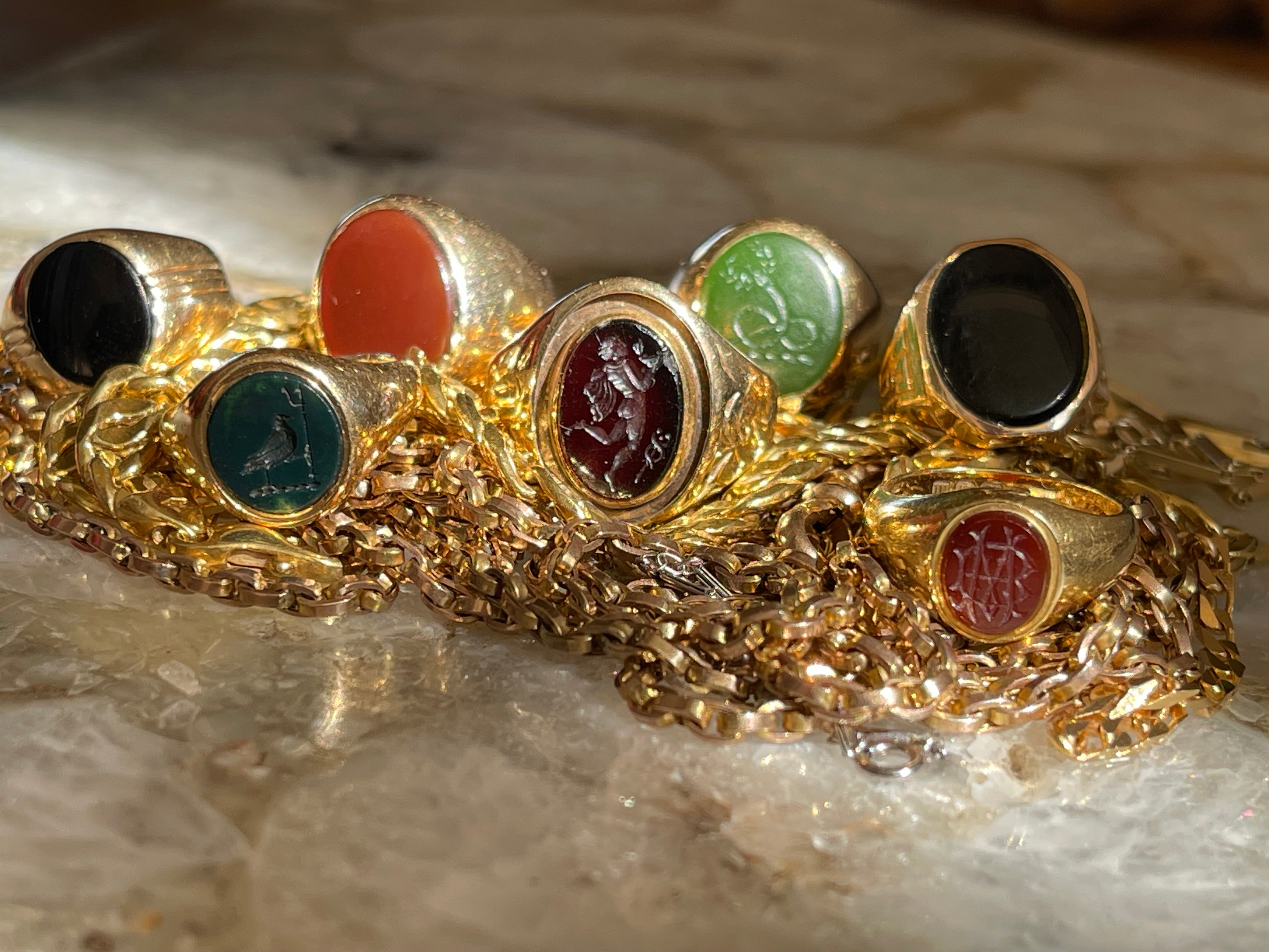 Signet rings on a pile of gold chains in golden light.